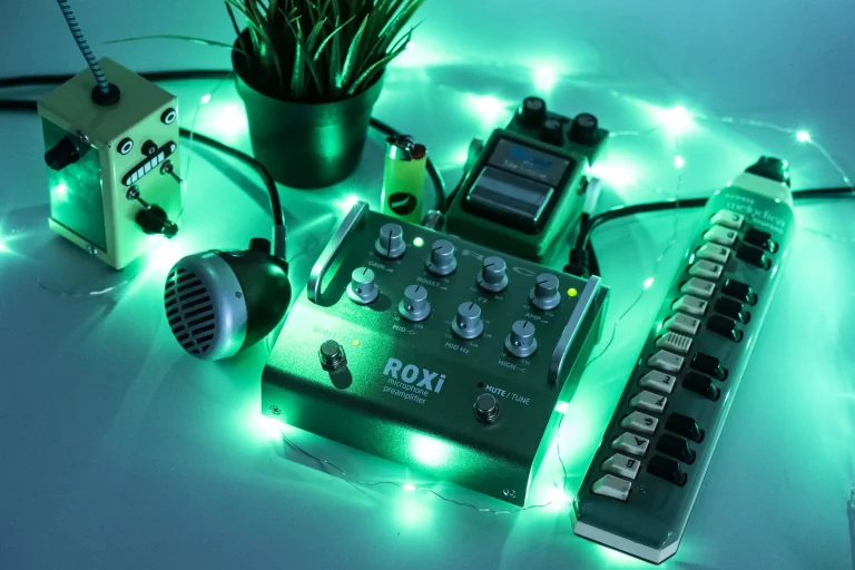 Grace Design ROXi microphone preamp pedal glowing under green stage lighting alongside performance accessories.